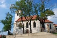 Kostel Narození sv. Jana Křtitele schován za stromy.