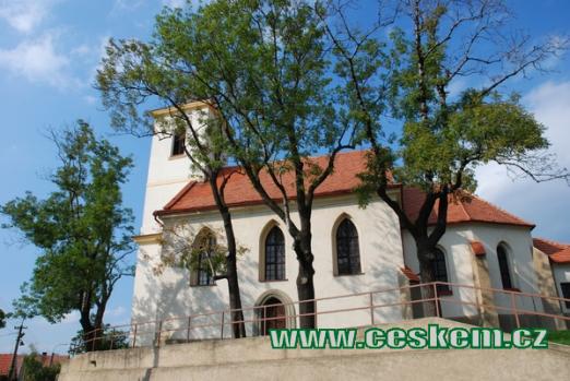 Kostel Narození sv. Jana Křtitele schován za stromy.
